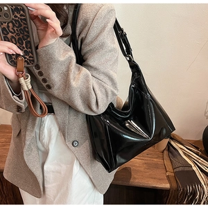 Détail du sac à bandoulière en similicuir noir brillant avec sangle réglable sur un tailleur