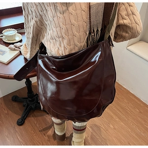 Detail view of a large dark brown saddle bag with glossy PU leather and wide shoulder strap