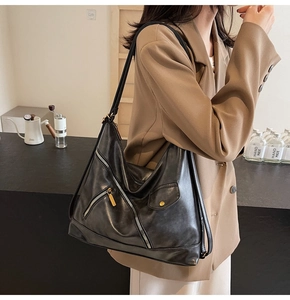 Detail of black PU leather hobo bag with zipper accents and gold hardware on a model