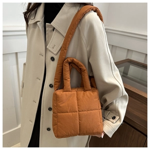 Detail of a bright orange quilted puffer tote bag styled with a beige trench coat