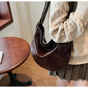 Detailed view of deep brown crescent shoulder bag in glossy leather on a model outfit