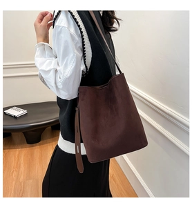Detail of a dark brown suede shoulder bucket bag featuring an adjustable wide strap for daily use