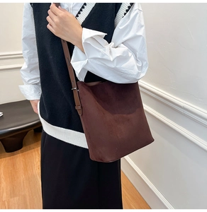Detail view of a large dark brown suede bucket bag with slim shoulder straps for women