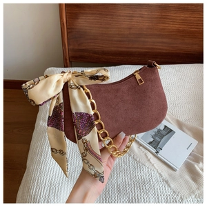 Detailed shot of brown suede shoulder bag with gold chain and patterned silk scarf accent