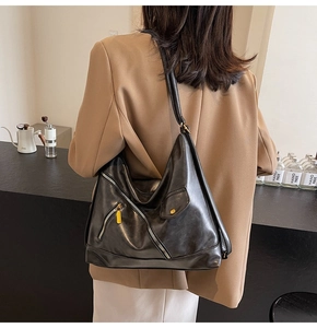 Detail of a black PU leather hobo bag with metal zippers and a yellow puller on wide strap