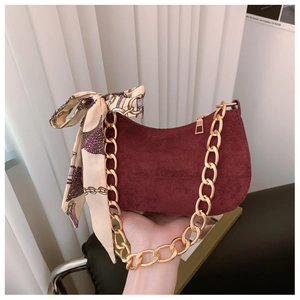 Close-up of burgundy suede crescent bag with gold chain strap and decorative silk scarf