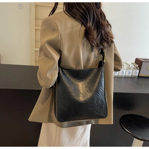 Detail of vintage black tote bag with wrinkled texture and golden buckle on model