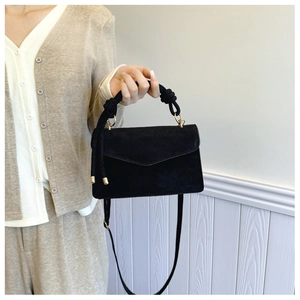 Close-up of black suede small square bag with knotted rope handle and golden buckle clasp