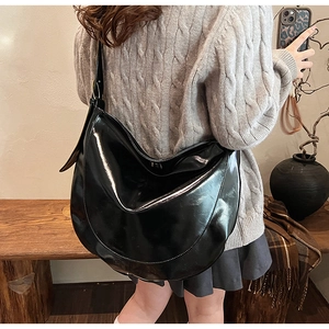 Polished black PU leather crescent moon shoulder bag with glossy finish on a model