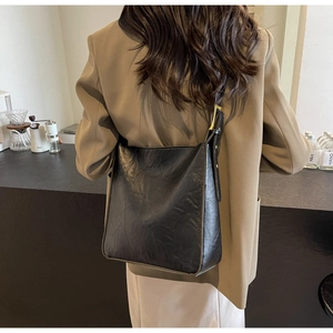Detail of classic black matte leather tote bag with adjustable strap worn by a model