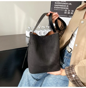 Detailed view of black suede bucket bag with wide shoulder strap in daily setting
