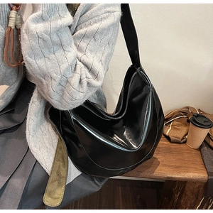 Fashionable black patent leather crescent bag shown on model for autumn street style