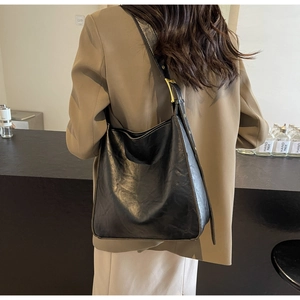 Modern black tote bag with vintage texture and golden hardware worn with camel blazer