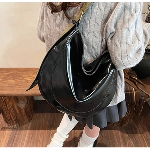 Detail of black glossy PU crescent bag with green wide shoulder strap and natural pleats