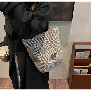 Detail of grey and yellow houndstooth tote bag with brown leather strap and logo patch