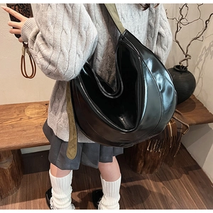Detail of glossy black PU leather hobo bag featuring a contrasting green suede strap