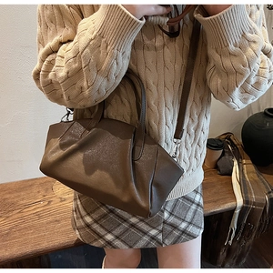 Detail of a dark brown pleated PU leather handbag with handles and a thin crossbody strap