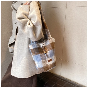 Detail of blue and brown checkered plush tote bag with leather logo tag on model