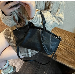 Detail of black vintage pleated PU leather handbag with round handle held by a model