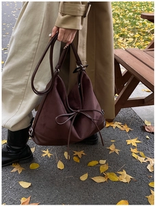 Close-up of a large dark brown matte PU tote bag with a decorative bow in an autumn park