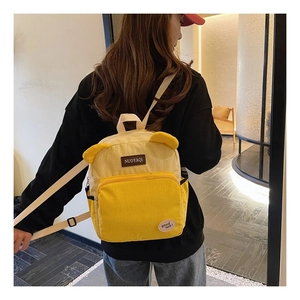 Detail view of yellow corduroy backpack with small ears and branded leather patch