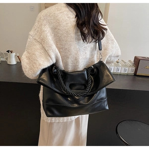 Detail of black large faux leather tote bag with braided handles shown in modern interior