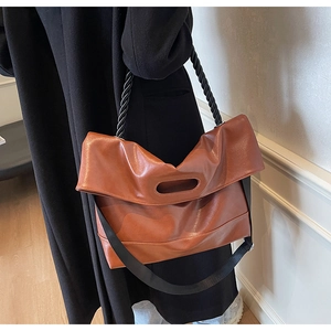 Brown soft PU leather handbag featuring unique twist handle and wide woven shoulder strap