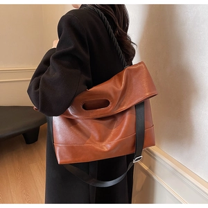 Detail of a brown vintage faux leather tote with unique oval cutout handle and woven strap