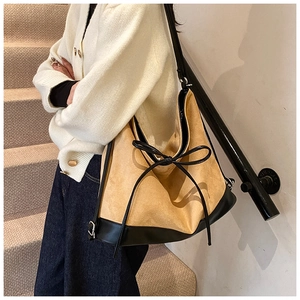Detail of ginger suede tote bag with black leather bow accent and long shoulder strap