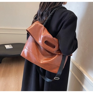 Close-up of brown faux leather shoulder bag with hollow handle and adjustable straps