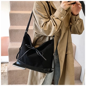 Detail of black tote bag featuring a leather bow accent and adjustable shoulder strap