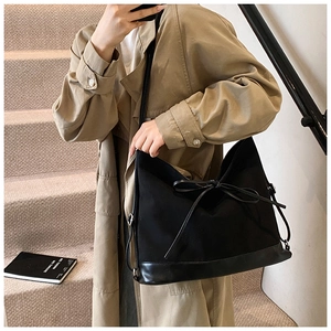 Detail of black tote bag with bow accent on a model wearing a khaki trench coat