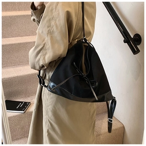 Detail of minimalist black drawstring tote bag with smooth leather base on khaki trench coat