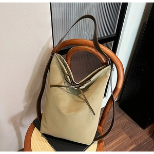 Sac seau tendance en daim kaki sable avec bandoulière en cuir marron sur une chaise en bois