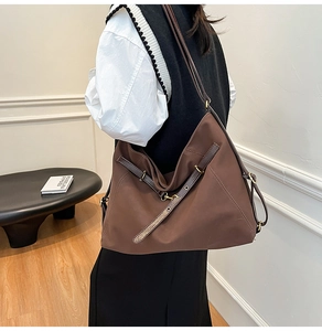Detail einer großen braunen Nylon-Tote-Tasche mit Lederriemen und Goldbeschlägen am Modell