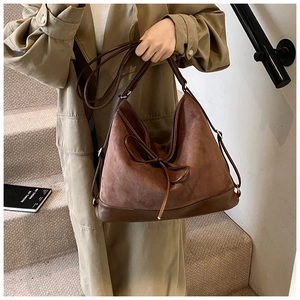 Detail of a large brown suede patchwork tote bag with a decorative bow on shoulder strap