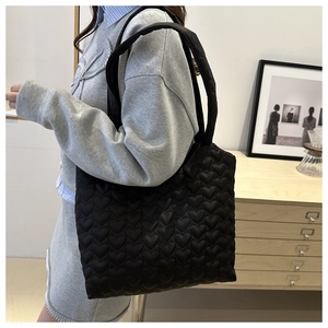 Détail de la couture matelassée en forme de cœur sur un sac cabas noir porté à l'épaule