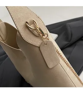 Detail of light beige suede handbag showing golden metal clasp and chain strap