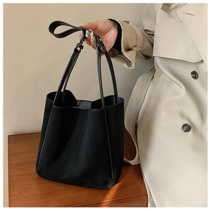 Détail d'un grand sac fourre-tout noir en similicuir mat tenu par une femme en trench beige