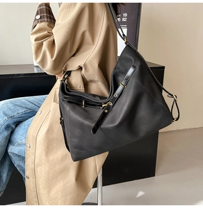 Große schwarze Einkaufstasche mit goldfarbenen Schnallen an Model im beigen Trenchcoat