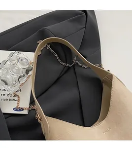 Detail of beige crescent shoulder bag with embossed logo and golden chain decoration