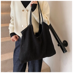 Close-up of black faux shearling tote bag with leather handles on a model in sunlight