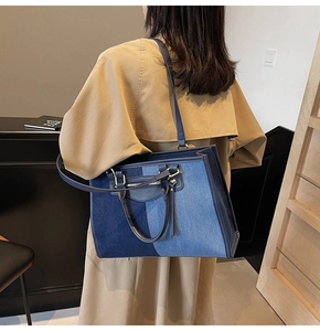 Detailed close-up of blue denim patchwork tote bag featuring golden zippers and leather straps