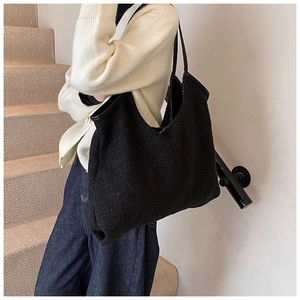 Detail of black fuzzy faux shearling tote bag with premium leather handles on model
