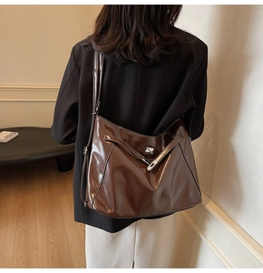 Détail d'un sac cabas en cuir brillant marron foncé avec boucle argentée porté par un modèle
