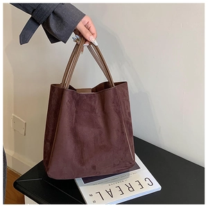 Gros plan sur la texture en daim marron mat et les fines anses en cuir du sac cabas