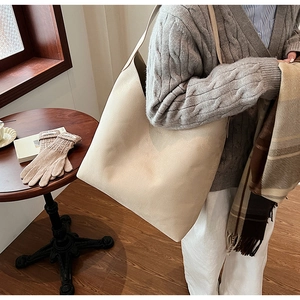 Close-up of a large beige soft PU leather tote bag worn over the shoulder in a cozy home setting
