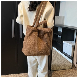 Close-up of soft brown plush tote bag texture with small woven label and shoulder strap