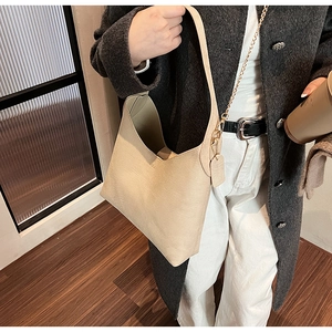 Detail of a beige hobo bag featuring wide straps and gold chain on a street style model