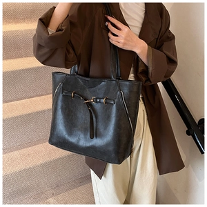 Deep black faux leather tote bag with gold metal buckles shown on model in a stylish setting